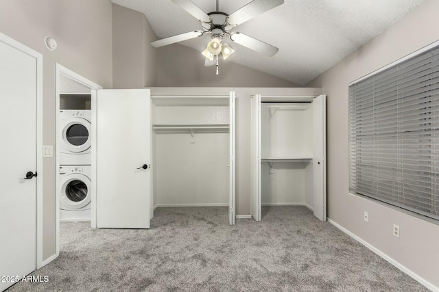 unfurnished bedroom with lofted ceiling, two closets, stacked washer and dryer, ceiling fan, and light colored carpet