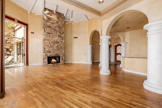 unfurnished living room with hardwood / wood-style floors, ceiling fan, a stone fireplace, ornate columns, and beam ceiling