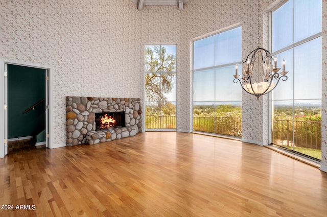 unfurnished living room with light wood-type flooring, a towering ceiling, a fireplace, and a notable chandelier