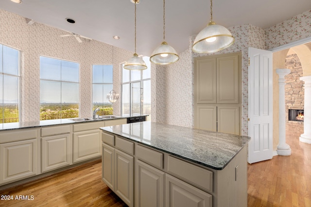 kitchen with a kitchen island, light stone countertops, a stone fireplace, light hardwood / wood-style floors, and sink