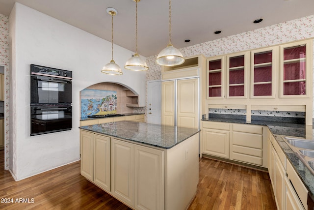 kitchen with cream cabinetry, gas stovetop, a center island, dark wood-type flooring, and black double oven