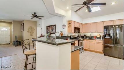 kitchen featuring a breakfast bar area, light brown cabinets, ceiling fan, and black appliances