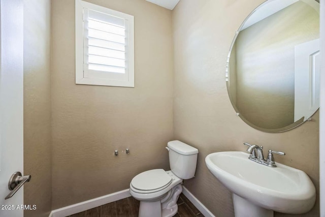 half bath with wood finished floors, a sink, toilet, and baseboards