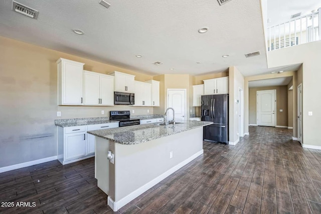 kitchen featuring visible vents, electric stove, stainless steel microwave, black fridge, and a sink