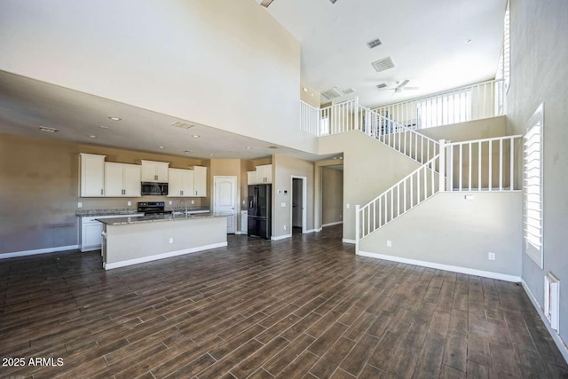 interior space featuring electric stove, dark wood-style flooring, black refrigerator with ice dispenser, open floor plan, and white cabinetry