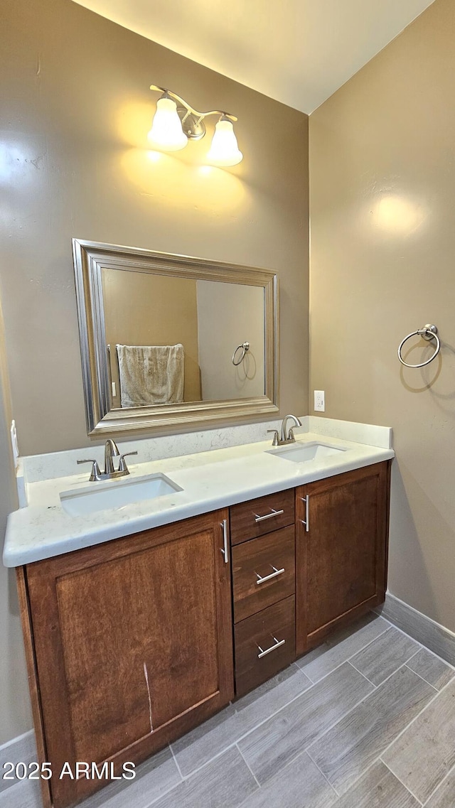 bathroom with double vanity, wood tiled floor, baseboards, and a sink