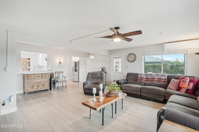 living room featuring ceiling fan, a wall unit AC, light hardwood / wood-style floors, sink, and a textured ceiling