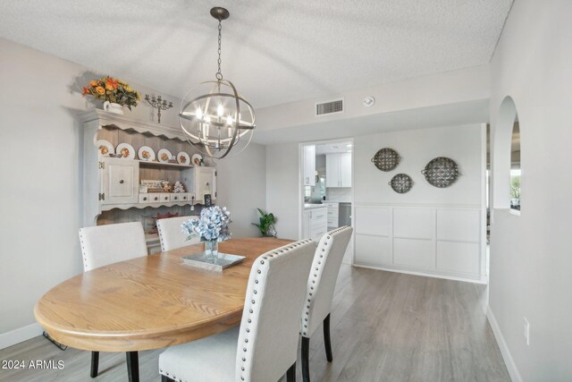 dining space featuring an inviting chandelier, light hardwood / wood-style flooring, and a textured ceiling