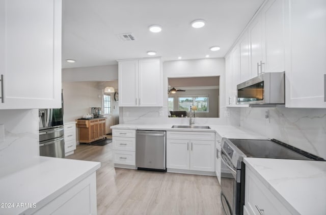 kitchen with light hardwood / wood-style flooring, tasteful backsplash, white cabinets, appliances with stainless steel finishes, and sink