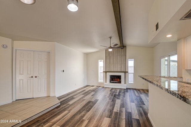 unfurnished living room with ceiling fan, a large fireplace, wood-type flooring, and lofted ceiling with beams