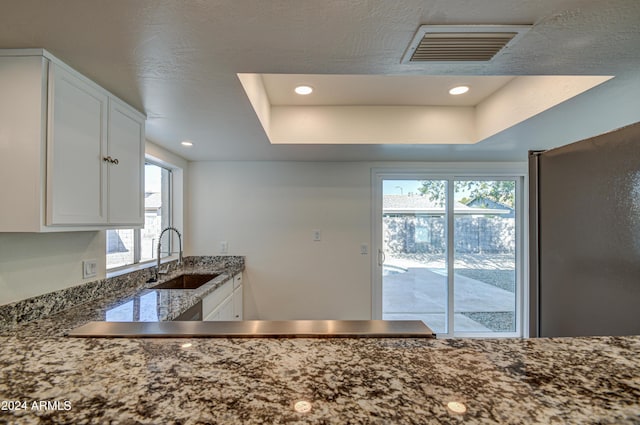 kitchen featuring white cabinetry, sink, a tray ceiling, and stainless steel refrigerator