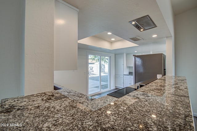 kitchen with stone counters, refrigerator, white cabinets, kitchen peninsula, and a raised ceiling