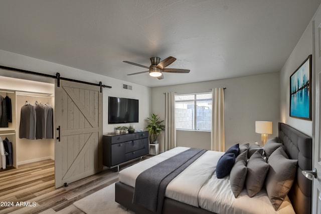 bedroom with ceiling fan, a barn door, hardwood / wood-style floors, and a walk in closet