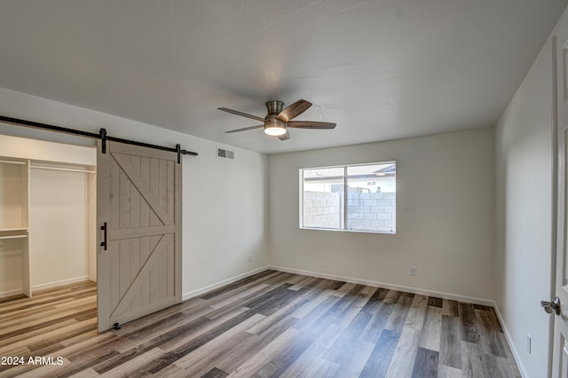 unfurnished bedroom with ceiling fan, a barn door, hardwood / wood-style floors, and a closet