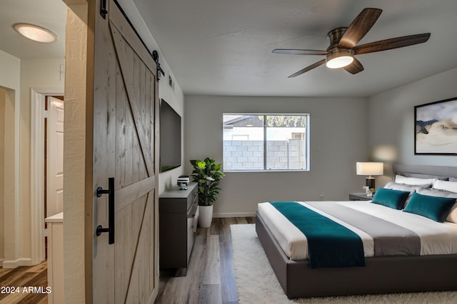 bedroom featuring ceiling fan, a barn door, and hardwood / wood-style floors