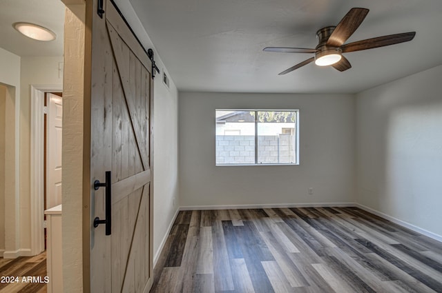 unfurnished room featuring ceiling fan, wood-type flooring, and a barn door