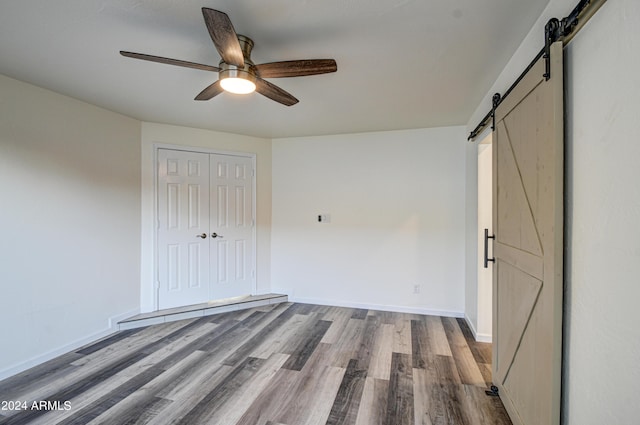 unfurnished bedroom with a closet, wood-type flooring, a barn door, and ceiling fan