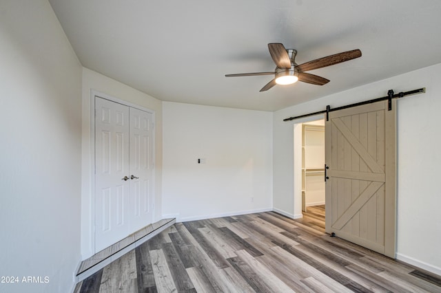 unfurnished bedroom with ceiling fan, a barn door, a closet, and light hardwood / wood-style flooring