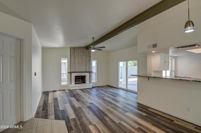 unfurnished living room featuring sink, ceiling fan, vaulted ceiling with beams, a fireplace, and dark hardwood / wood-style flooring