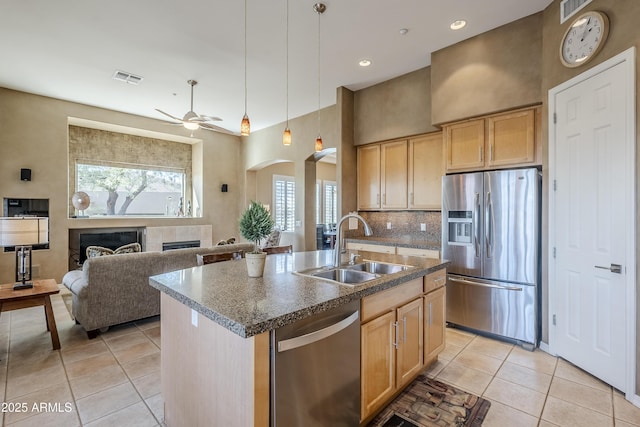 kitchen with sink, a center island with sink, light brown cabinets, stainless steel appliances, and a tiled fireplace