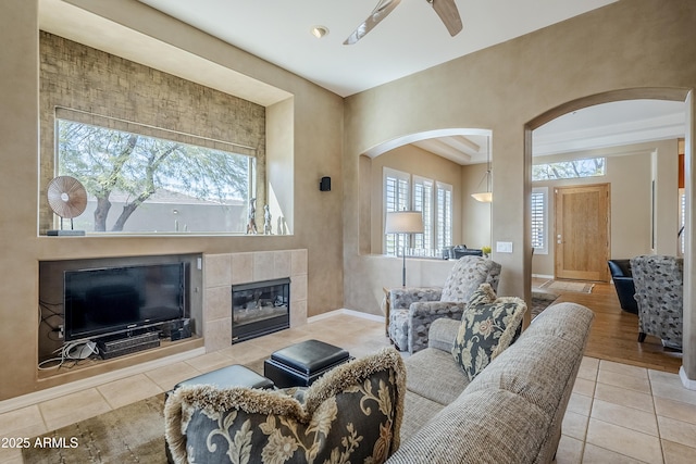 living room with ceiling fan, a tile fireplace, a healthy amount of sunlight, and light tile patterned flooring