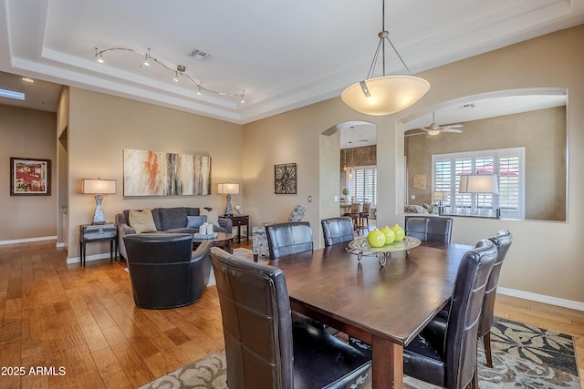 dining space featuring a tray ceiling, light hardwood / wood-style flooring, rail lighting, and ceiling fan