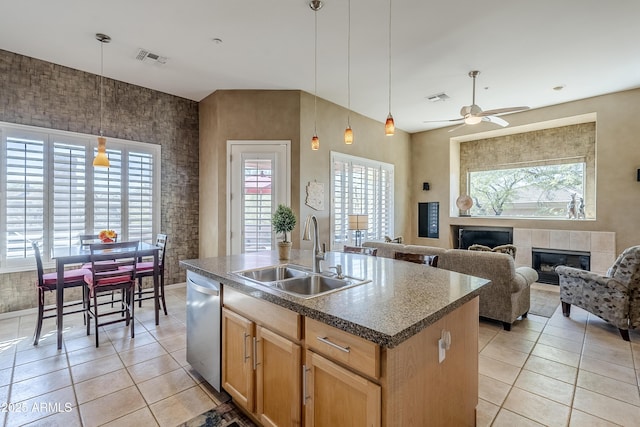 kitchen featuring a fireplace, dishwasher, an island with sink, sink, and light tile patterned floors