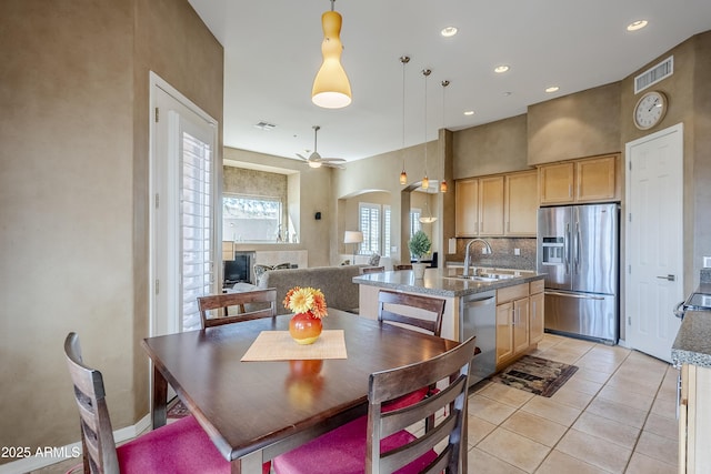 kitchen with hanging light fixtures, appliances with stainless steel finishes, a center island with sink, and light brown cabinets