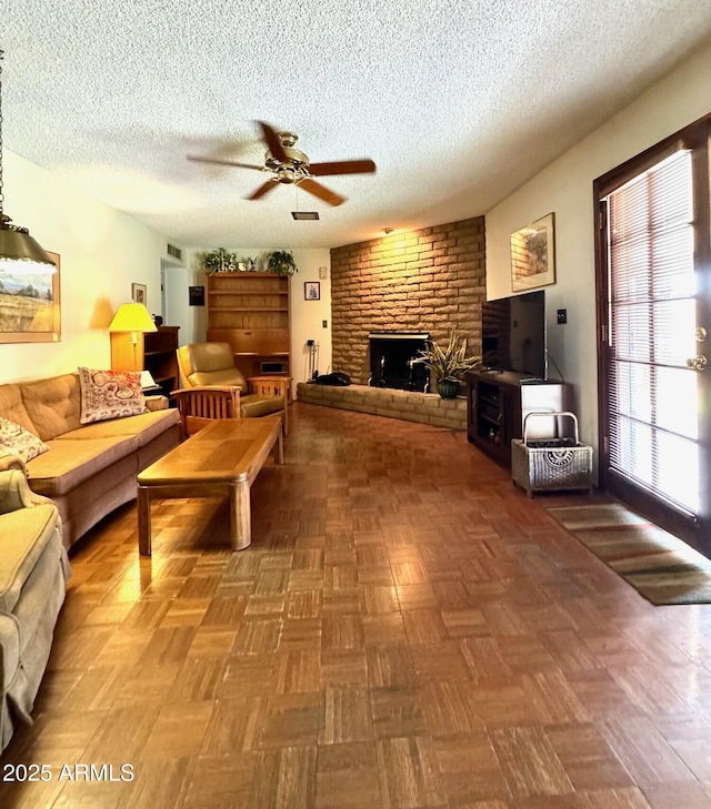 living area featuring a brick fireplace, a textured ceiling, visible vents, and ceiling fan