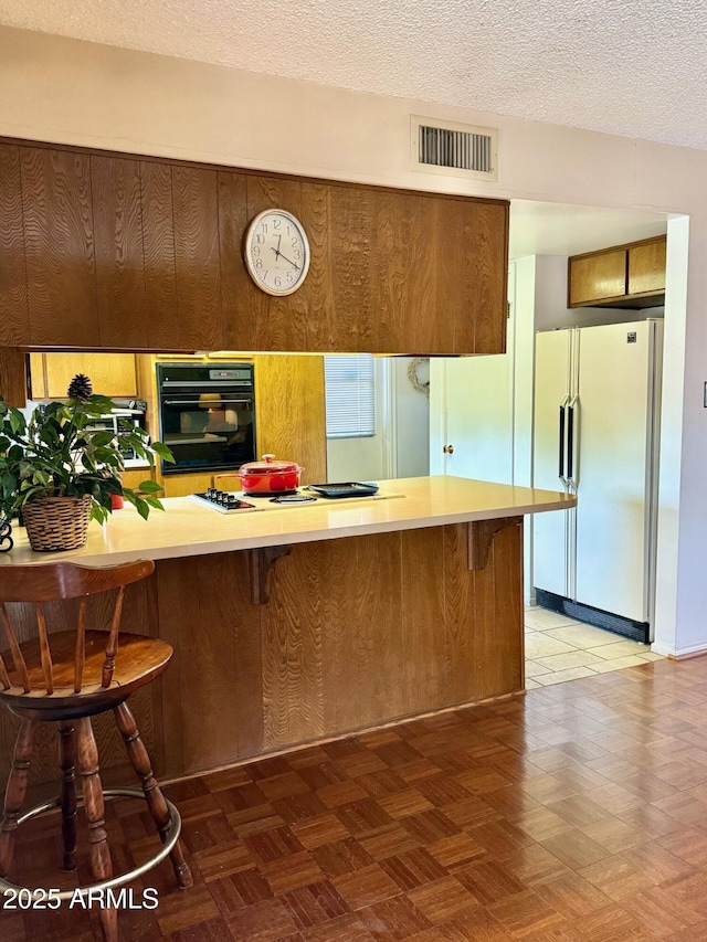 kitchen featuring white appliances, light countertops, a textured ceiling, visible vents, and a kitchen bar