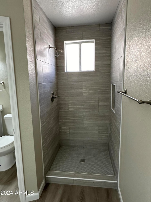 bathroom featuring wood-type flooring, a textured ceiling, a tile shower, and toilet