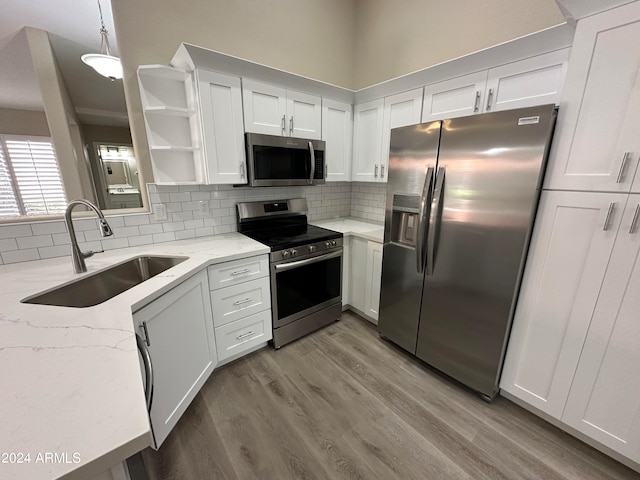 kitchen featuring hanging light fixtures, light stone counters, light hardwood / wood-style flooring, white cabinets, and appliances with stainless steel finishes