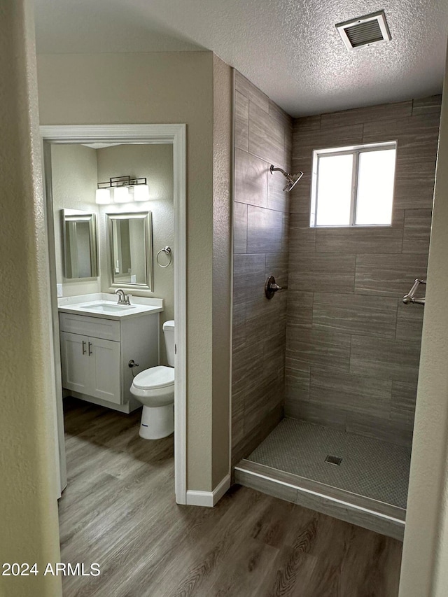 bathroom with a tile shower, vanity, a textured ceiling, hardwood / wood-style floors, and toilet