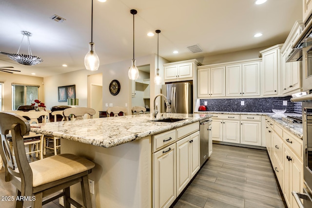 kitchen with pendant lighting, an island with sink, appliances with stainless steel finishes, tasteful backsplash, and a kitchen bar