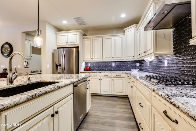 kitchen with light stone countertops, decorative light fixtures, stainless steel appliances, and wall chimney range hood