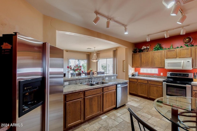 kitchen featuring light stone countertops, appliances with stainless steel finishes, track lighting, sink, and decorative light fixtures