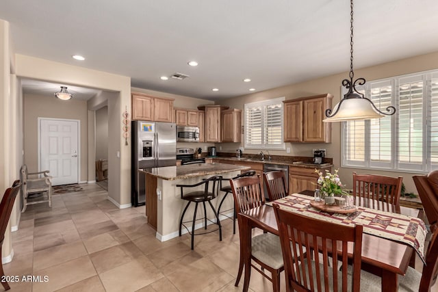 kitchen with a kitchen island, sink, dark stone countertops, hanging light fixtures, and stainless steel appliances