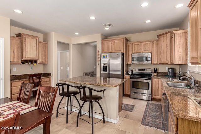 kitchen with sink, light tile patterned floors, a breakfast bar area, appliances with stainless steel finishes, and dark stone countertops