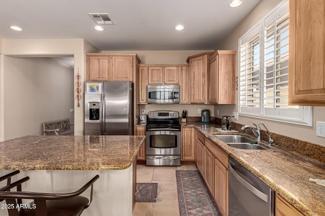 kitchen with light tile patterned flooring, appliances with stainless steel finishes, stone countertops, sink, and a breakfast bar area