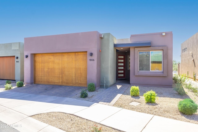 southwest-style home featuring a garage, decorative driveway, and stucco siding