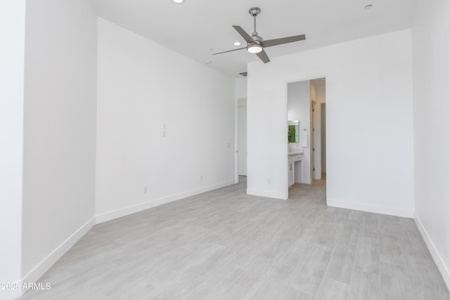 unfurnished bedroom featuring baseboards, a ceiling fan, ensuite bath, light wood-style flooring, and a spacious closet