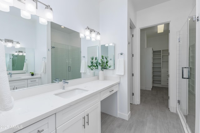 full bathroom featuring vanity, a shower stall, a walk in closet, and baseboards