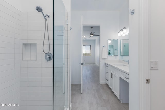 full bathroom featuring a tile shower, vanity, baseboards, and wood finished floors