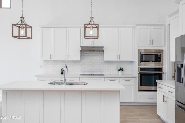 kitchen with white cabinets, decorative backsplash, appliances with stainless steel finishes, under cabinet range hood, and a sink