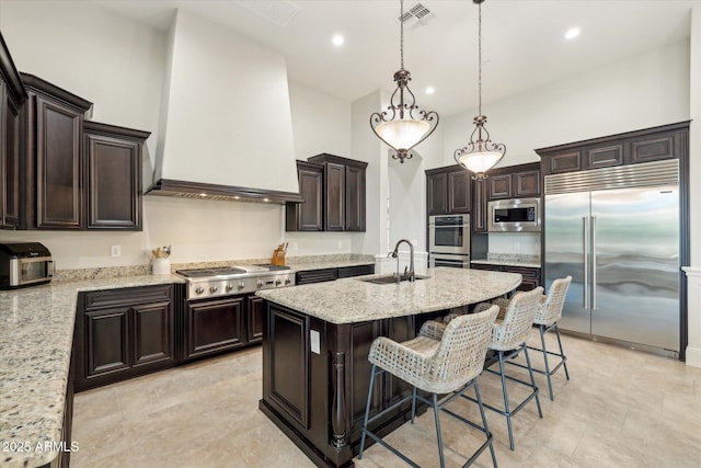 kitchen with premium range hood, visible vents, a kitchen island with sink, a sink, and built in appliances