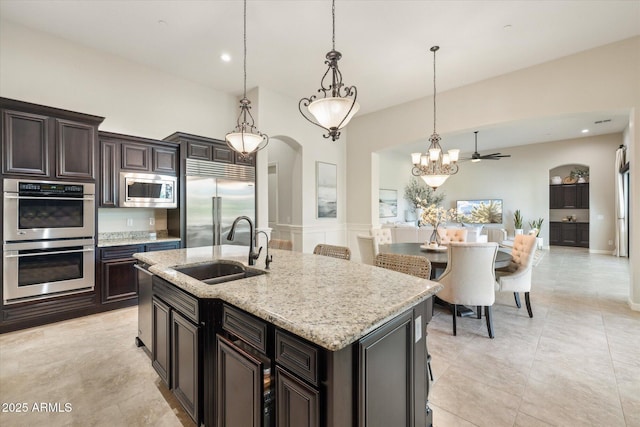 kitchen featuring light stone counters, an inviting chandelier, a sink, hanging light fixtures, and built in appliances