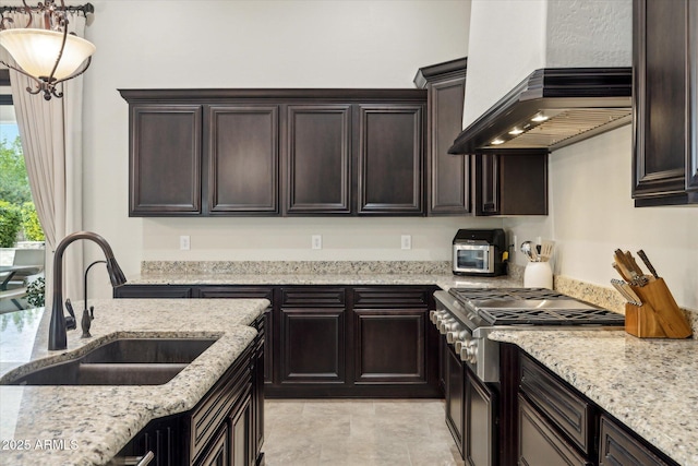 kitchen with a sink, dark brown cabinets, stainless steel gas stovetop, and wall chimney range hood