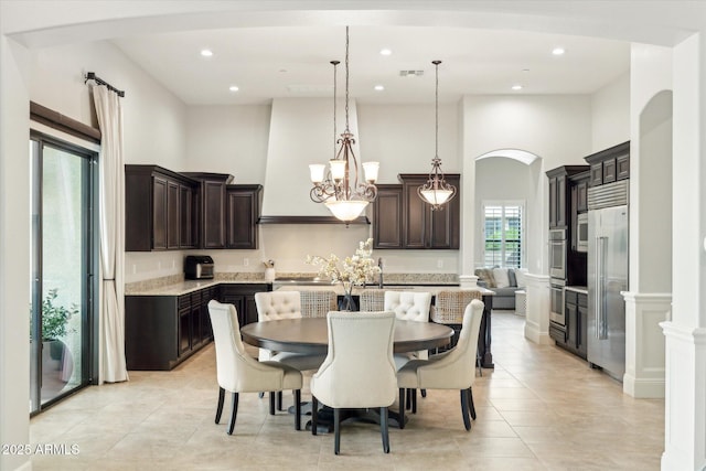 dining space with light tile patterned floors, visible vents, arched walkways, and a towering ceiling