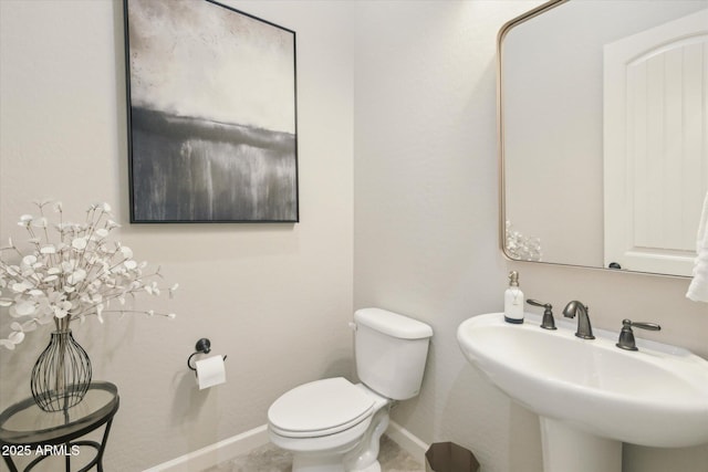 half bath featuring toilet, baseboards, and a sink