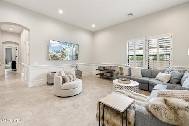 living room featuring arched walkways, a decorative wall, wainscoting, and visible vents